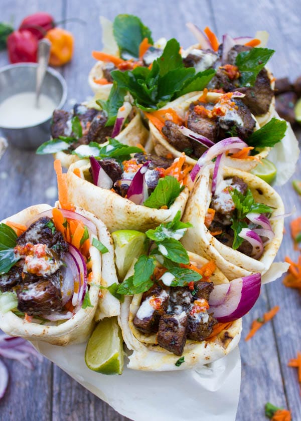 pita cones filled with grilled harissa lamb shoulder, grated carrots, lettuce and drizzled with Tahini sauce served in rectangular metal pan on a rustic wood table.