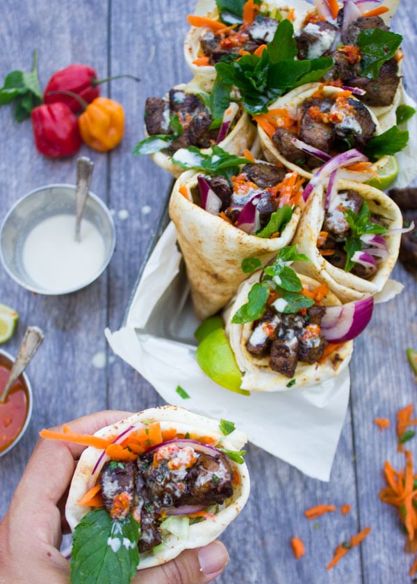 a hand holding a pita cone filled with charred lamb shoulder, grated carrots, fresh herbs and red onion slices with a drizzle of tahini sauce on top.