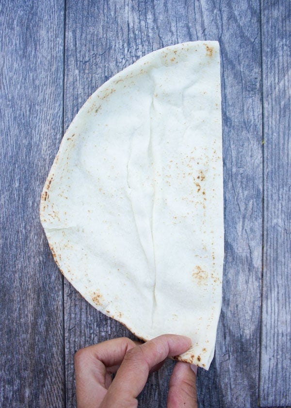 pita bread folded in half placed on a rustic table to demonstrate shaping of pita cones.