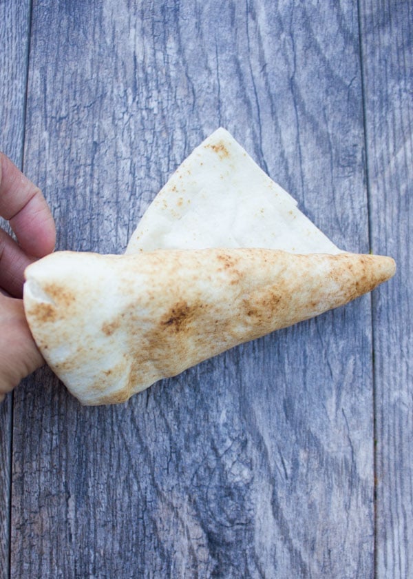 a pita bread being rolled up into a pita cone on a rustic wooden table.