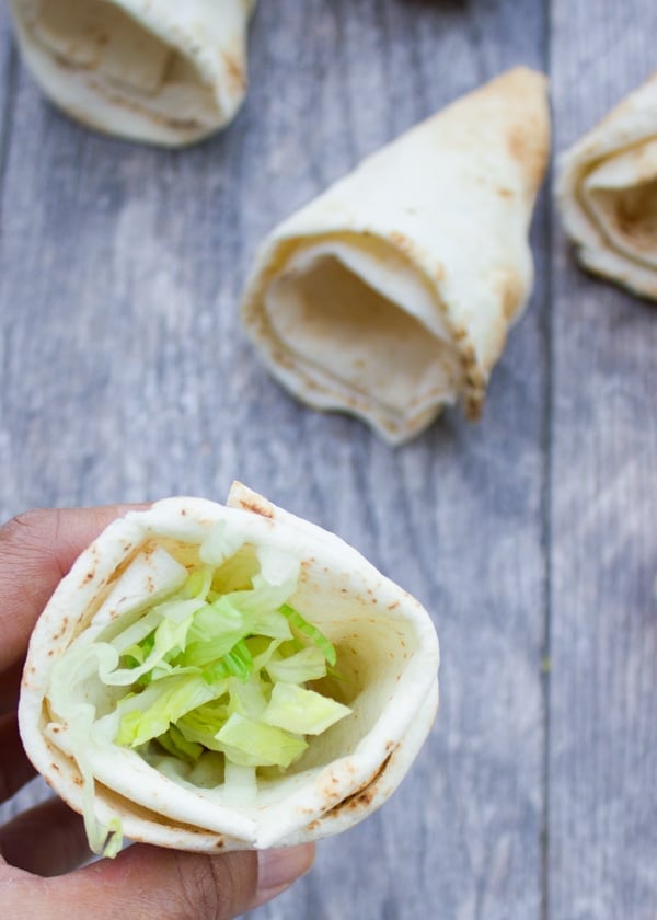 hand holding a pita cone filled with shredded lettuce.