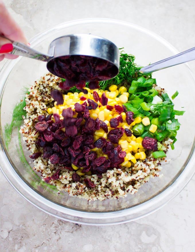 dried cranberries being added to quinoa stuffing ingredients in a glass bowl