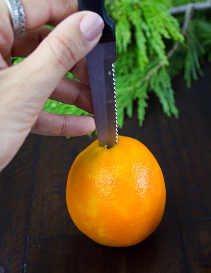 a tiny slit being cut into an orange to insert a rosemary twig