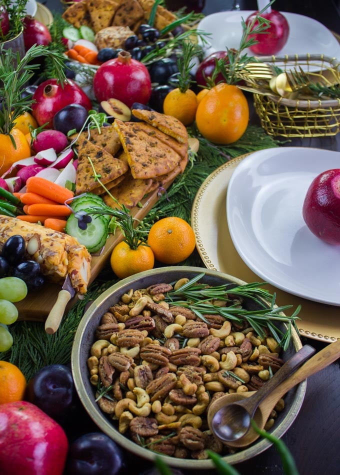 Rosemary Spiced Candied Pecans and Pita Chips arranged on a table with seasonal fruit and plates for a Cheese Party. 