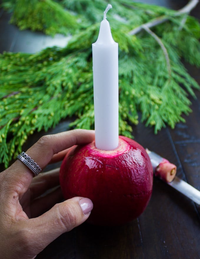 a candle being inserted into a pomegranate to make a candleholder