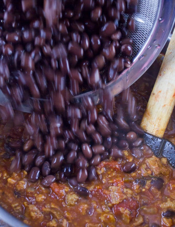 black beans being added to a pot with vegetarian chili