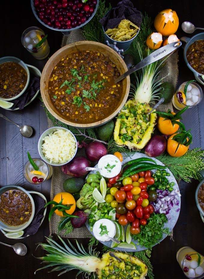overhead shot of a pot of a table loaded with Vegetarian Chili, salsa-stuffed pineapples and a veggie platter