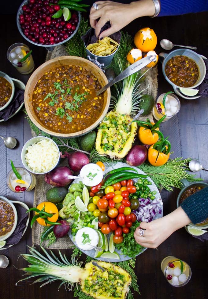 overhead shot of a table with a pot of Vegetarian Chili, filled pineapples and a veggie platter