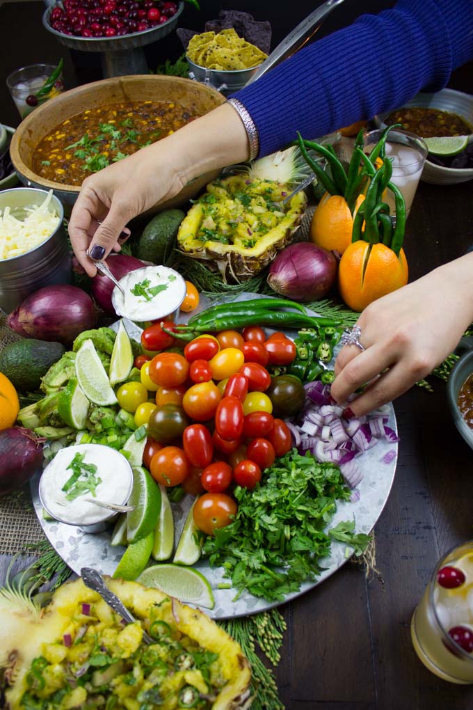 several hands reaching out for ingredients on a chili bar 