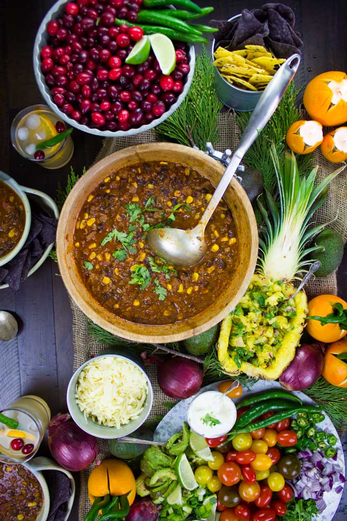 overhead shot of a table with a pot of Vegetarian Chili, a veggie platter, a bowl of cranberries and pineapple salsa