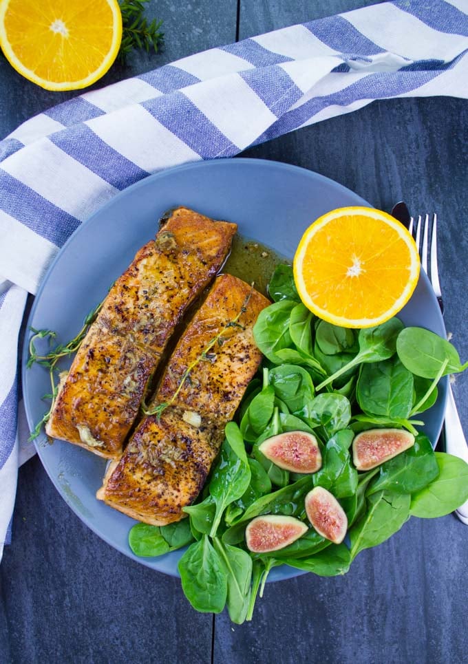 two Garlic Orange Pan-Seared Salmon fillets on a blue plate with a side salad