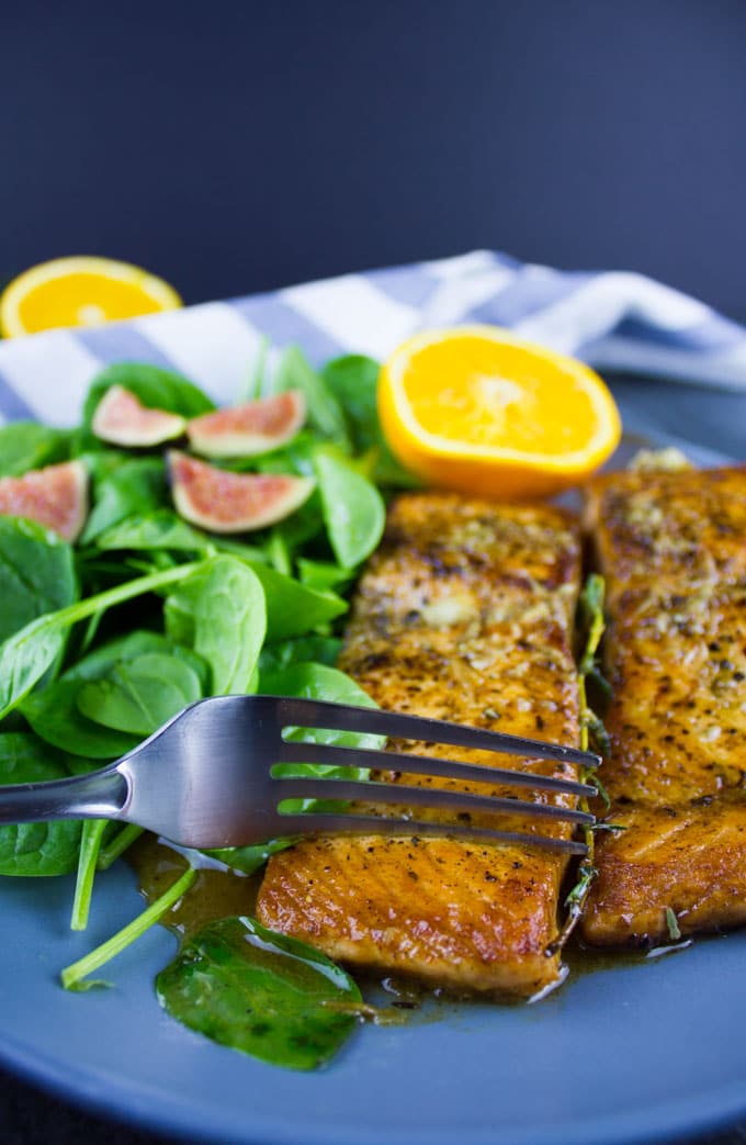 a fork breaking of a small piece of pan-seared salmon fillet with garlic and orange