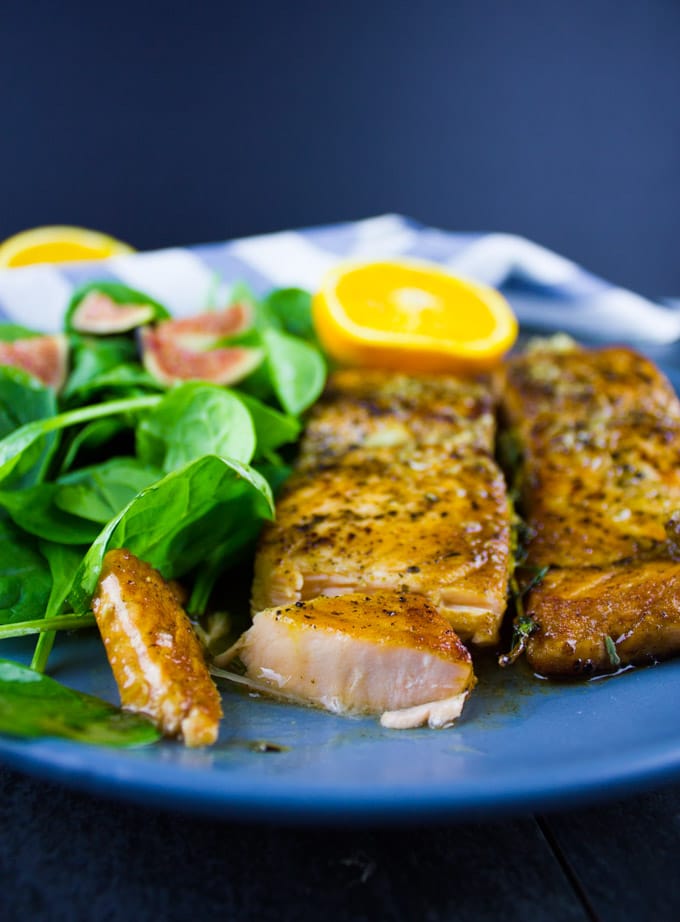 side view of two pan-seared Garlic Orange Salmon fillets on a blue plate with a side salad