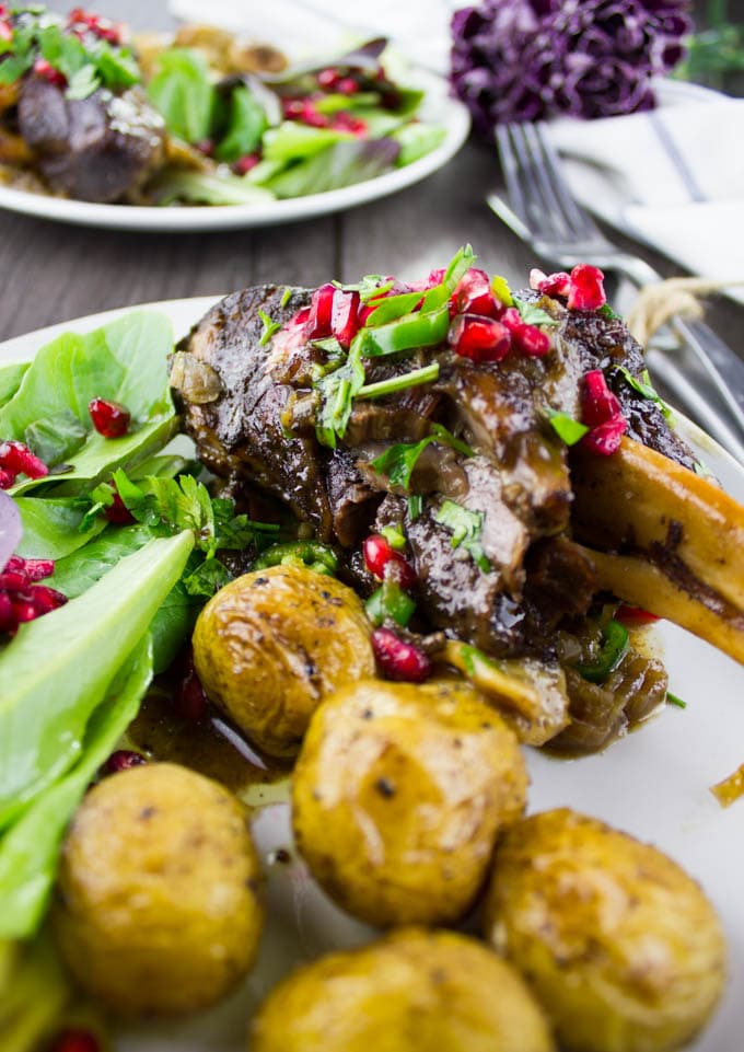 side view of Pomegranate Roast Lamb Shanks with potatoes and a side salad on a plate