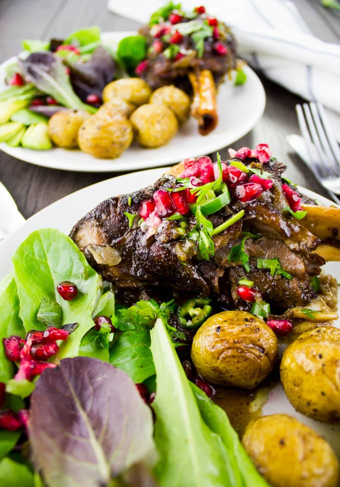 close-up of a plate of Pomegranate Roasted Lamb Shanks with potatoes and a salad