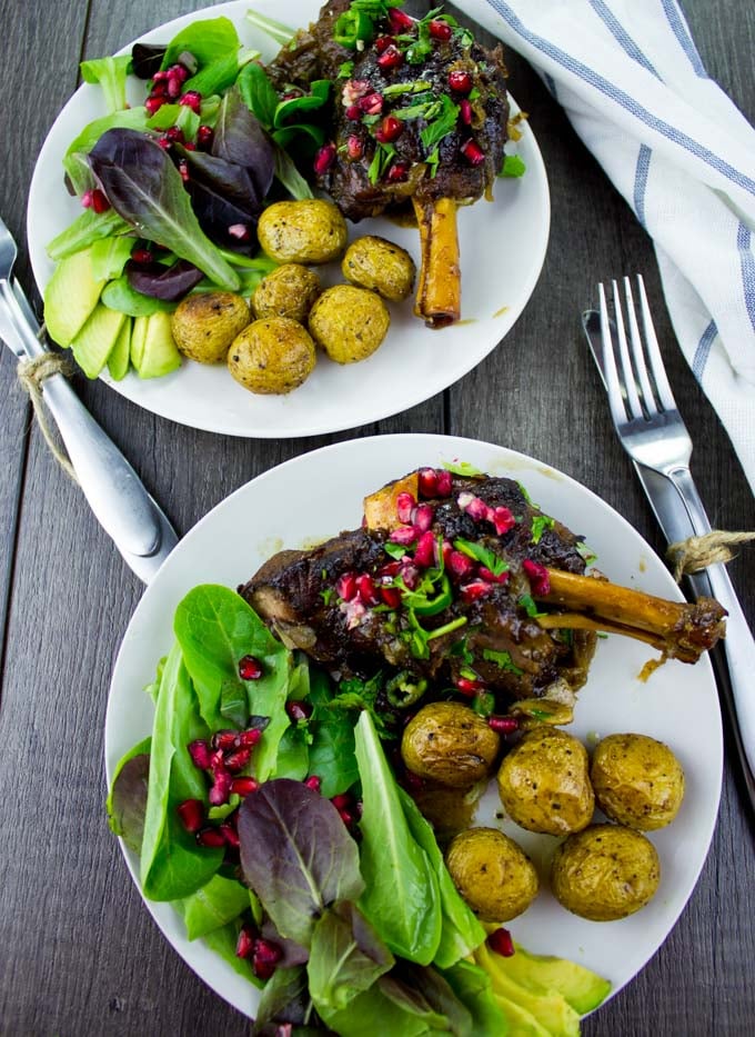 overhead shot of two plates of Pomegranate Roast Lamb Shanks with potatoes and a side salad