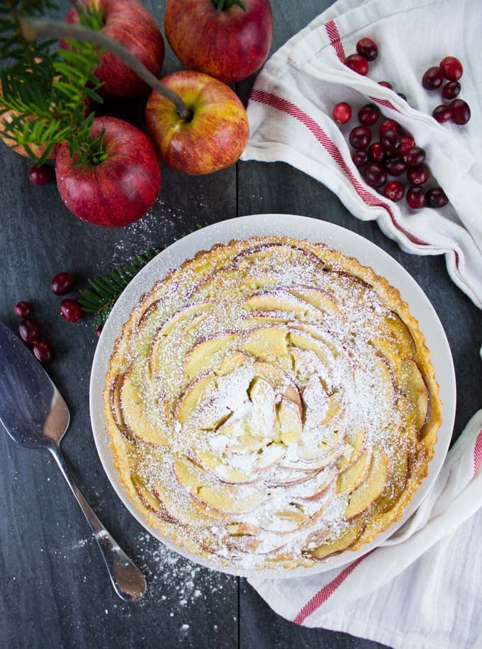 overhead shot or Swiss Apple Tart dusted with icing sugar and surrounded with apples and cranberries