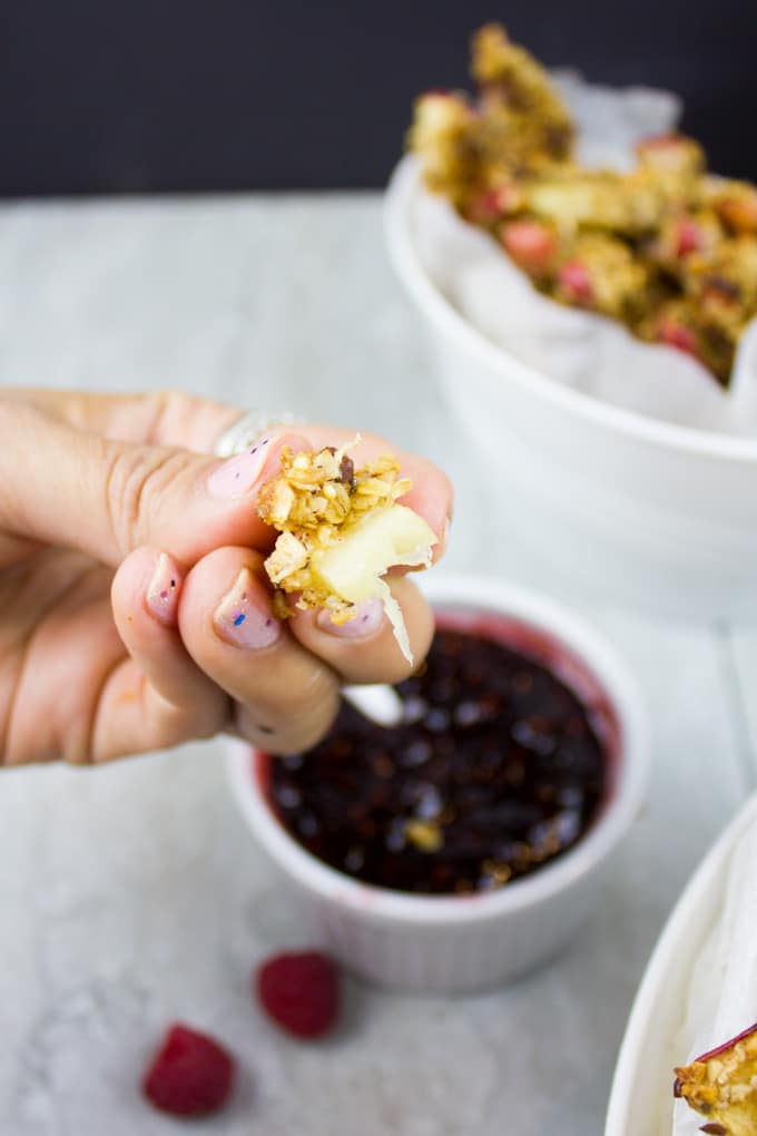 a hand holding a Baked Apple Fry With Raspberry Sauce with bite taken out the front