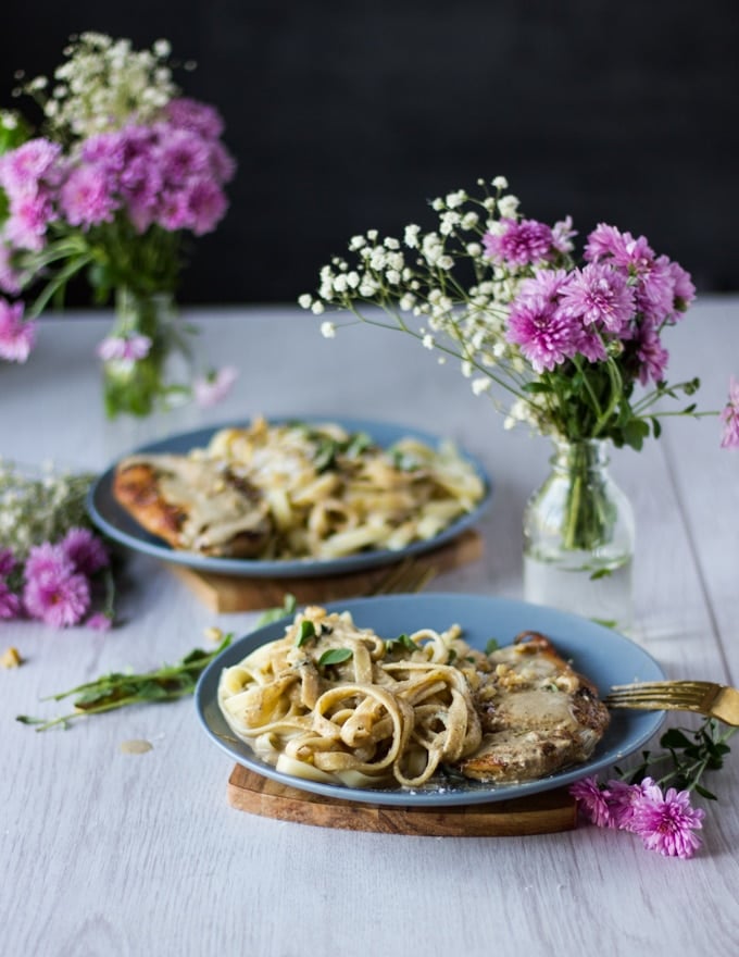 two plates of winner winner chicken dinner with pan seraed chicken breasts and wlanut sauce over pasta. Some pink flowers surrounding the plates