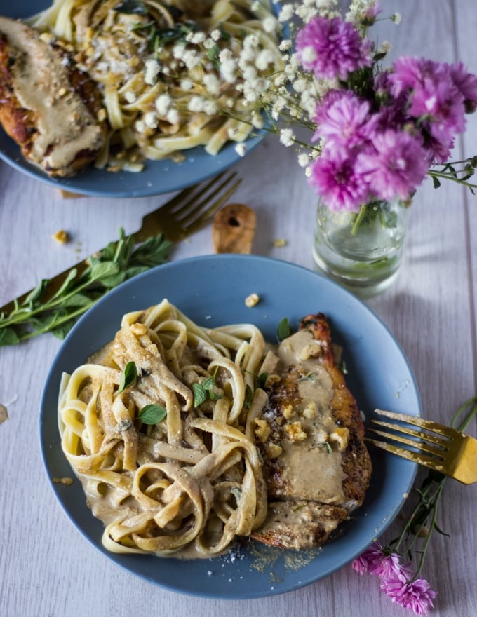 A single plate of the chicken dinner showing the pasta on one side drenched in walnut sauce and the chicken on the other side. A fork is shown on the side of the plate and a small vase of flowers. 