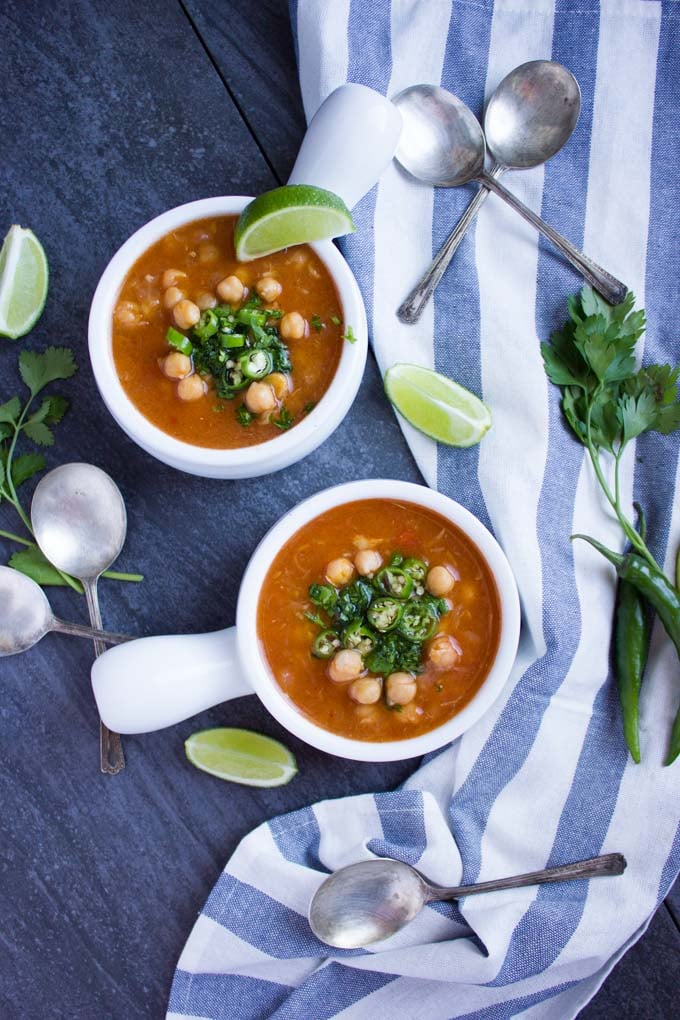 overhead shot of two small bowls of Soothing Garlic Chickpea Soup topped with sliced green chilies 