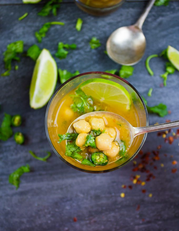 a spoon being dunked into a glass of Turkish garlic and chickpea soup 