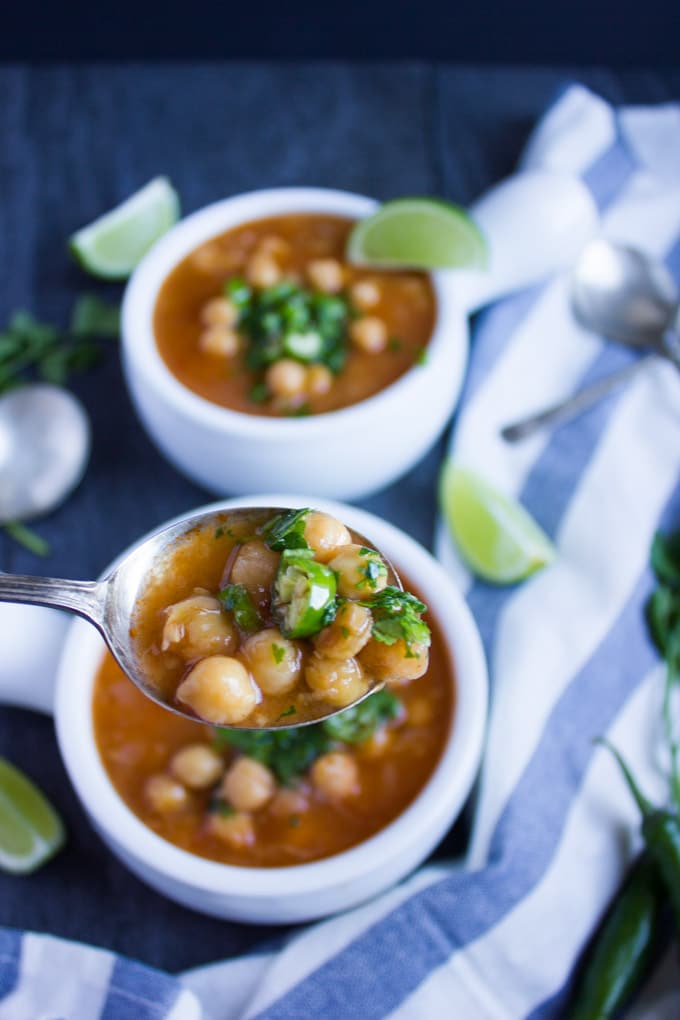 a spoon with Garlic Chickpea Soup being balanced over a white soup bowl