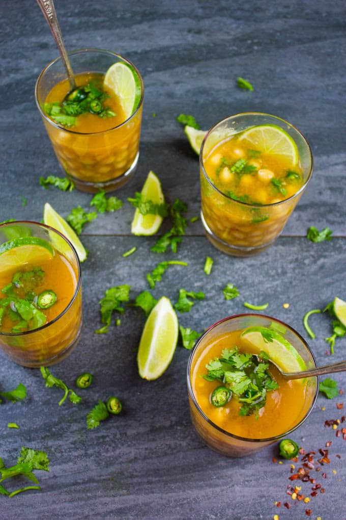 overhead shot of four glass cups of Soothing Garlic Chickpea Soup topped with green chilies and cilantro