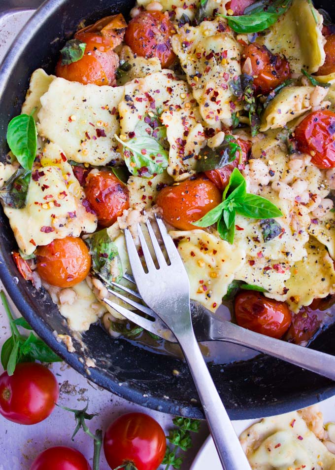 15 Minute One Pan Ravioli with navy beans and mini tomatoes sprinkled with chili flakes and fresh basil served in a black skillet