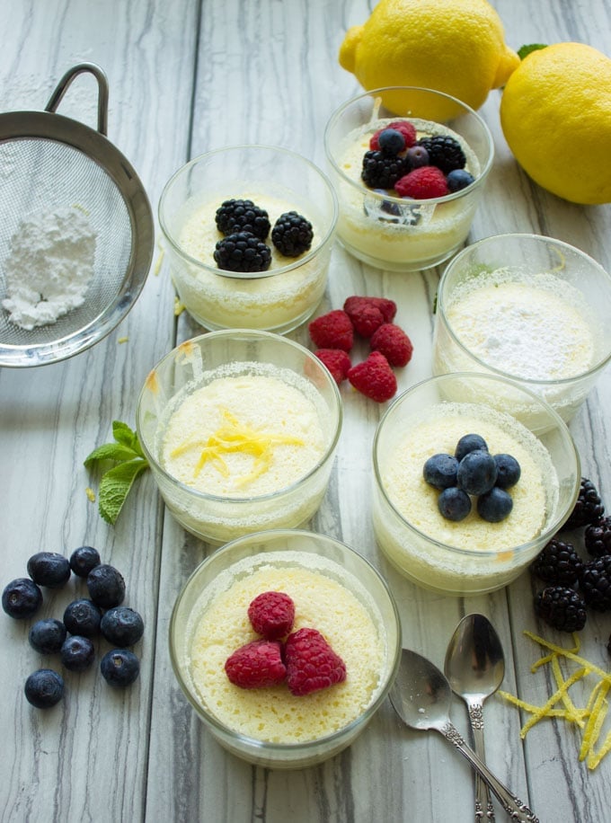 overhead shot of Easy Mini Lemon Pudding Cakes in dessert glasses topped with berries and icing sugar