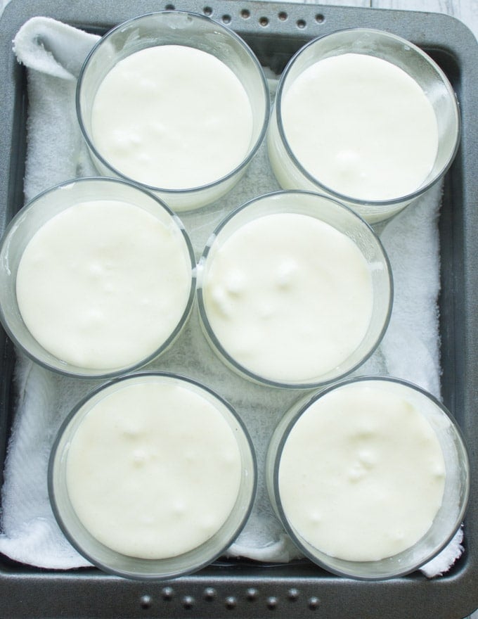 a tray of mini lemon pudding cakes in dessert glasses ready to bake in a water bath