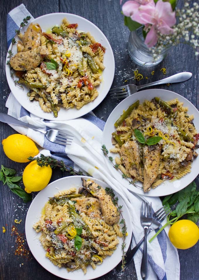 overhead shot of three plates of creamy one-pot chicken pasta with fresh lemons on the side