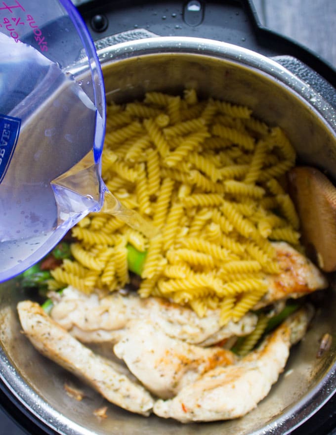 pasta and water being added to chicken and vegetables in an instant pot