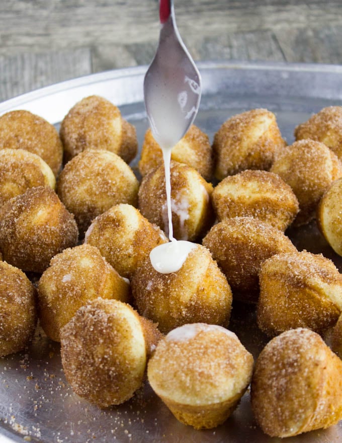 vanilla glaze being drizzled on top of cinnamon sugar dusted donuts.