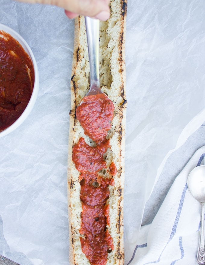 marinara sauce being spread on a crusty toasted ciabatta loaf