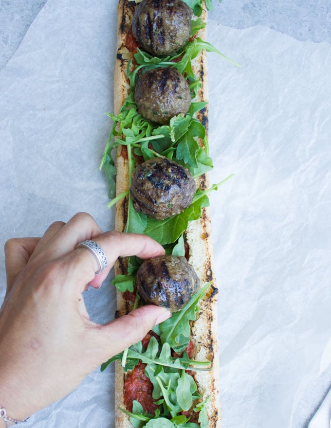 grilled lamb meatballs being lined up on top of open-faced sandwich