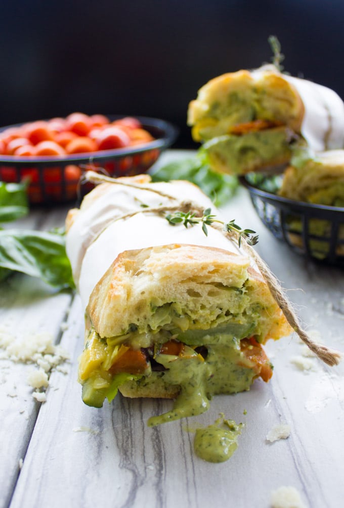 close-up of half a Roasted Veggie Sandwich with Basil Sauce on a rustic white table with some sauce dripping down the sides of the bread