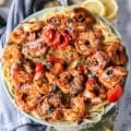 close up of a plate of shrimp pasta with the shrimp on top with herbs, baby tomatoes some feta cheese and lemon slices