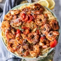close up of a plate of shrimp pasta with the shrimp on top with herbs, baby tomatoes some feta cheese and lemon slices