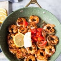 lemon slices, baby tomatoes cut up, butter knobs, herbs and more garlic are added to the cooked shrimp