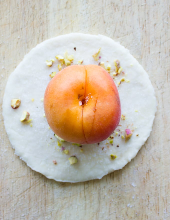 a whole apricot being placed in the middle of a pie pastry round