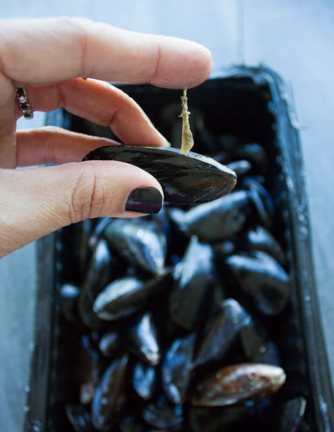 A hand pulling off a thread off the mussels to clean the mussels before cooking.