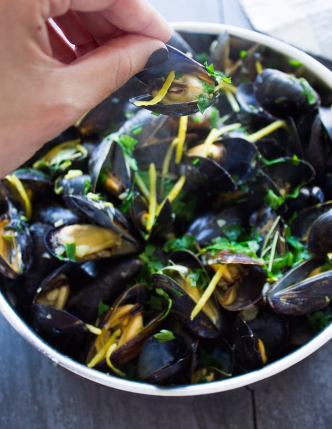 A hand holding a cooked mussels close up showing the steam and flavors in the mussels.