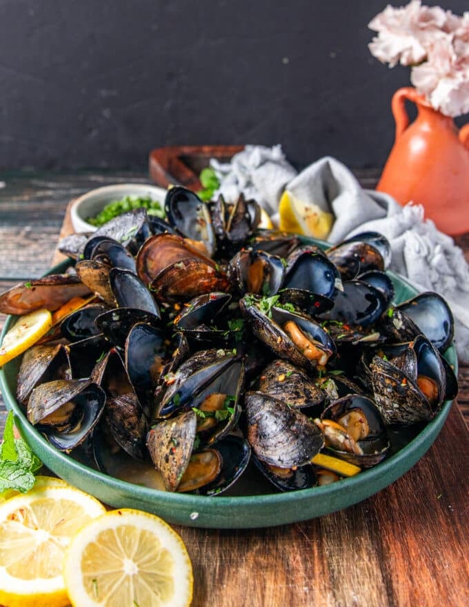 Side view of a plate of cooked mussels showing the tender meat and broth