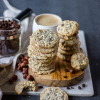 Stacks of coffee cookies on a wooden board with a large cup of coffee in the background