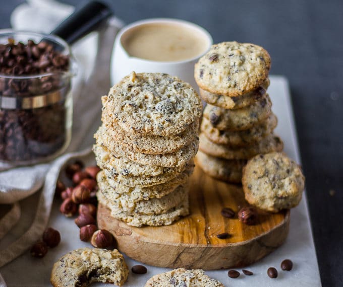 Stacks of coffee cookies on a wooden board with a large cup of coffee in the background