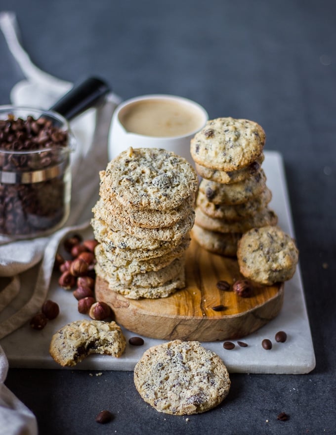 Stacks of coffee cookies on a wooden board with a large cup of coffee in the background