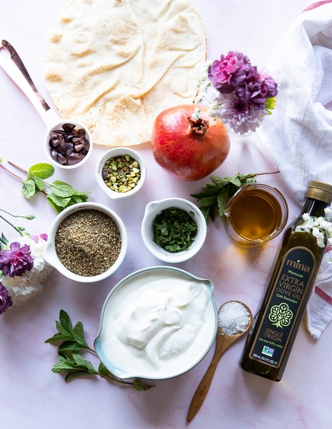 Ingredients to make labneh with a zaatar topping using moroccan olive oil, zaatar, pistachio, mint, and pomegranate