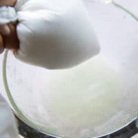 A hand squeezing the pillowcase very strongly to remove the water out of the yogurt