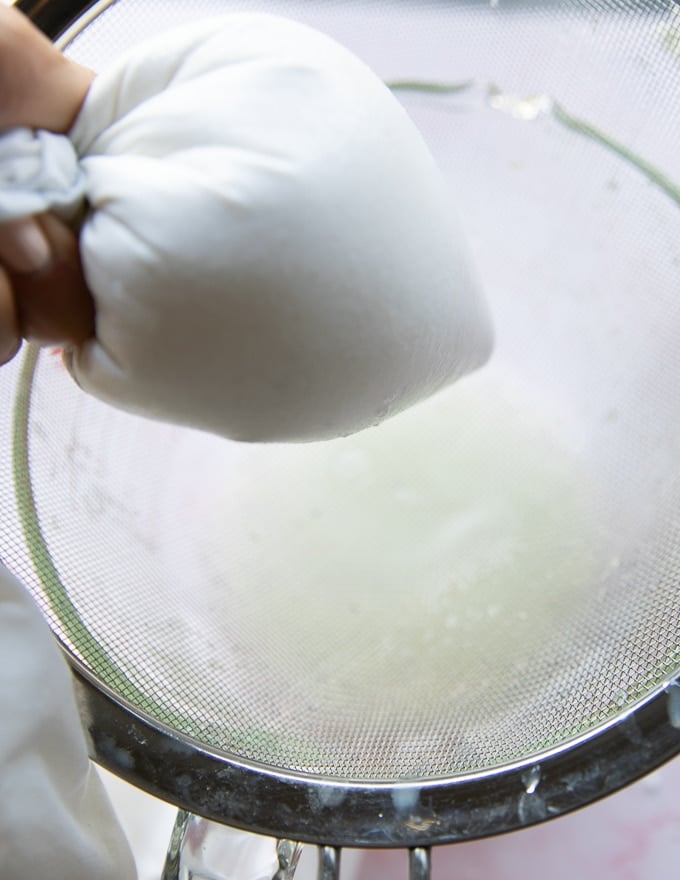 A hand squeezing the pillowcase very strongly to remove the water out of the yogurt